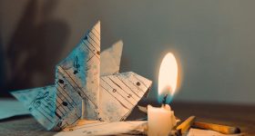 An artistic setting of a paper origami swan made from sheet music, beside a lit candle and matches.