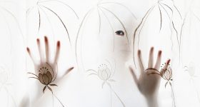 Artistic silhouette of a person with hands and eye visible through a decorative curtain.